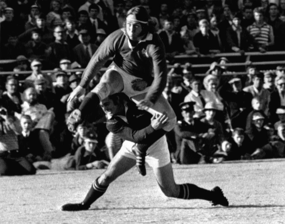 FILE - British Lions winger J.P.R. Williams gets his foot to the ball despite the efforts of Springbok Chris Pope in the test match at Loftus Versfeld, Pretoria, on June 22, 1974. JPR Williams, the Wales rugby great of the 1970s known for his fearlessness and swashbuckling attacking style, has died. He was 74. His death was announced Monday Jan. 8, 2024 by Bridgend Ravens, a club that Williams served as a player and club president. (AP Photo/File)