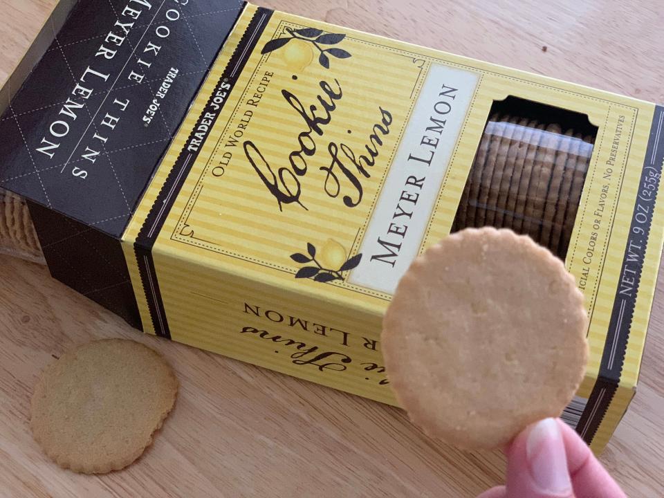 hand holding trader joe's meyer lemon cookie beside black and yellow box