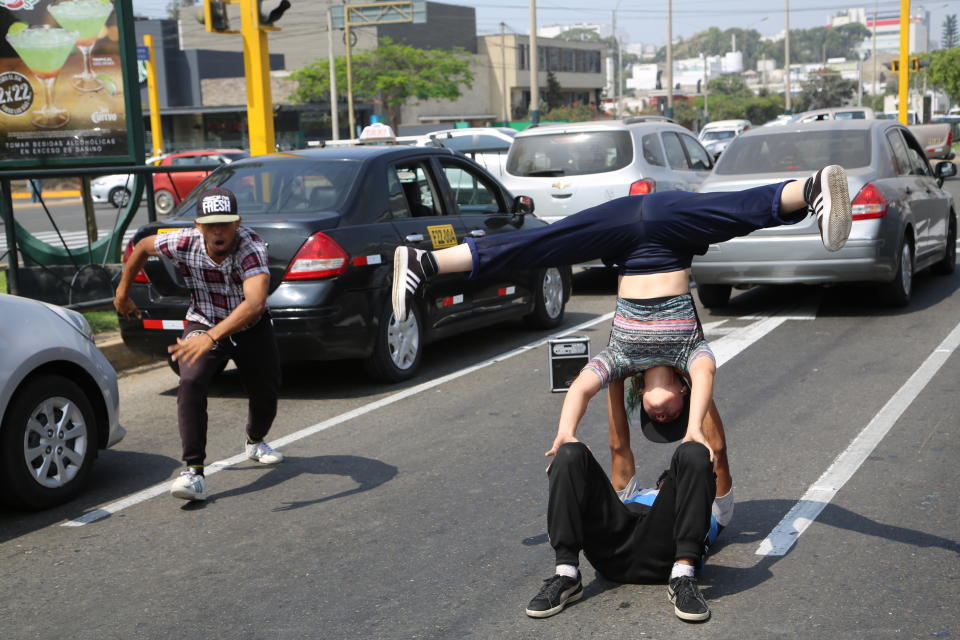 In this Dec. 12, 2018 photo, Venezuelan breakdancers Maria Molina, right, Alex Beltran, on the ground, and Miguel Angel Flores perform for tips from commuters in Lima, Peru. With a captive audience of pedestrians and commuters, the dancers' headstands, spins and steps on a good day net up to $20 in pocket change, nearly three times the monthly minimum wage in Venezuela. (AP Photo/Cesar Olmos)
