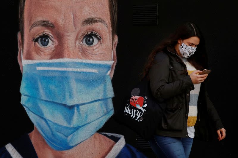 A woman wears a face mask as she walks past a mural of a nurse following the outbreak of the coronavirus disease (COVID-19) in Manchester, Britain