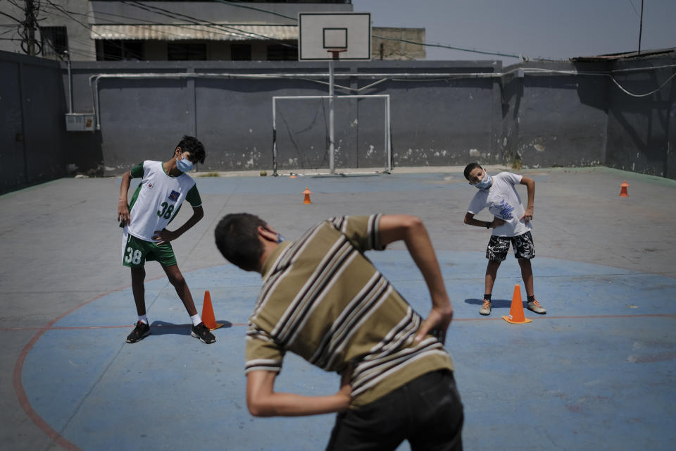 Children wearing protective face masks as a measure to curb the spread of the new coronavirus, stretch their muscles before they play a game of soccer, in the Lidice neighborhood of Caracas, Venezuela, Saturday, May 16, 2020. President Nicolas Maduro is relaxing quarantine measures over the weekend by allowing children and older adults out of their homes for a few hours each day. (AP Photo/Matias Delacroix)