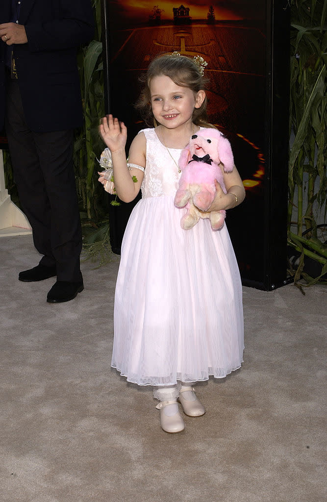 Young girl in a flowing dress poses with a plush toy on the red carpet