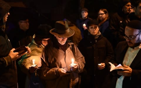 People hold candles outside the Tree of Life Synagogue after a shooting there left 11 people dead in the Squirrel Hill neighbourhood of Pittsburgh  - Credit: AFP