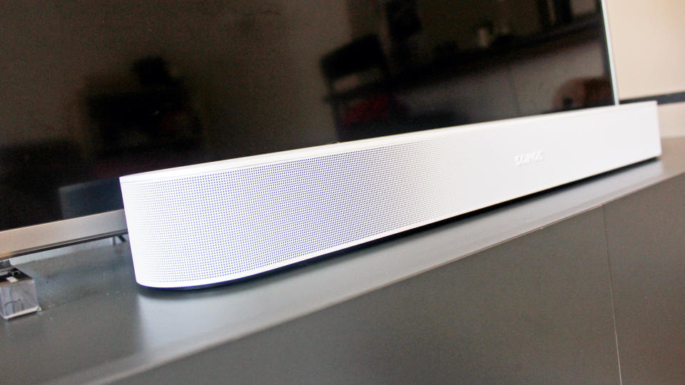 the sonos beam gen 2 soundbar in white pictured on a TV cabinet under a TV screen