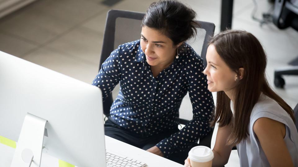 Multiracial colleagues indian and caucasian young women having coffee break sitting together at desk in office.