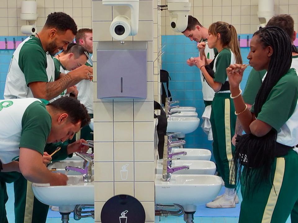 squid game the challenge players brush their teeth at sinks in a brightly colored  blue and cream tiled bathroom