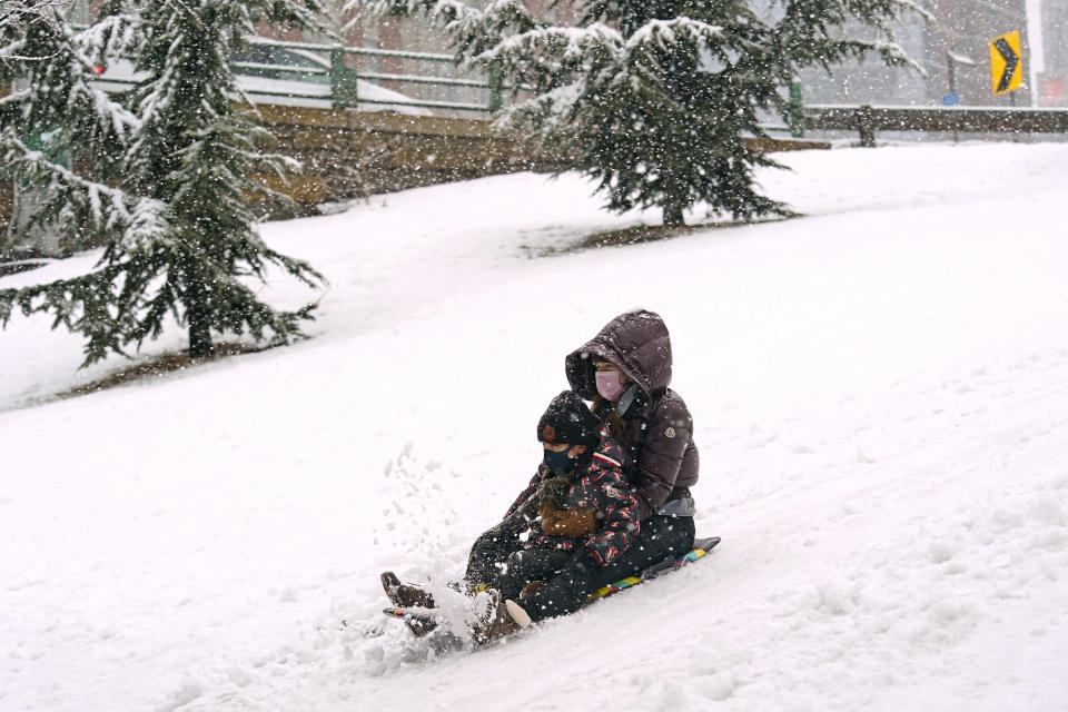 A woman and child ride a snowboard down a small hill in downtown Brooklyn during a snowstorm, Sunday, Feb. 7, 2021, in New York. It was the second snowstorm to hit the New York area in less than a week. (AP Photo/Kathy Willens)