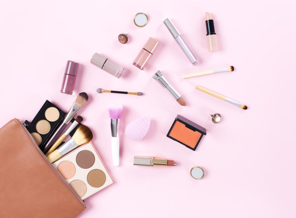 Makeup bag with cosmetic products spilling out on to a soft pink background