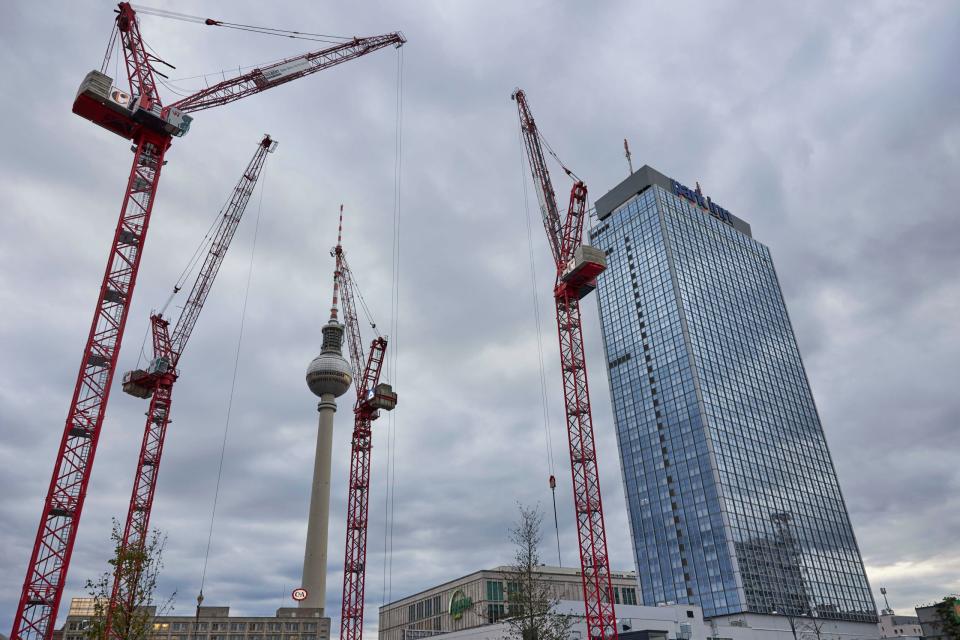 Vier große Baukräne ragen vor dem Fernsehturm und dem Park Inn Hotel in den Himmel impor. Die Kräne sind Teil einer Baustelle, auf der ein Hochhaus gebaut wird. - Copyright: picture alliance / Jörg Carstensen | Joerg Carstensen