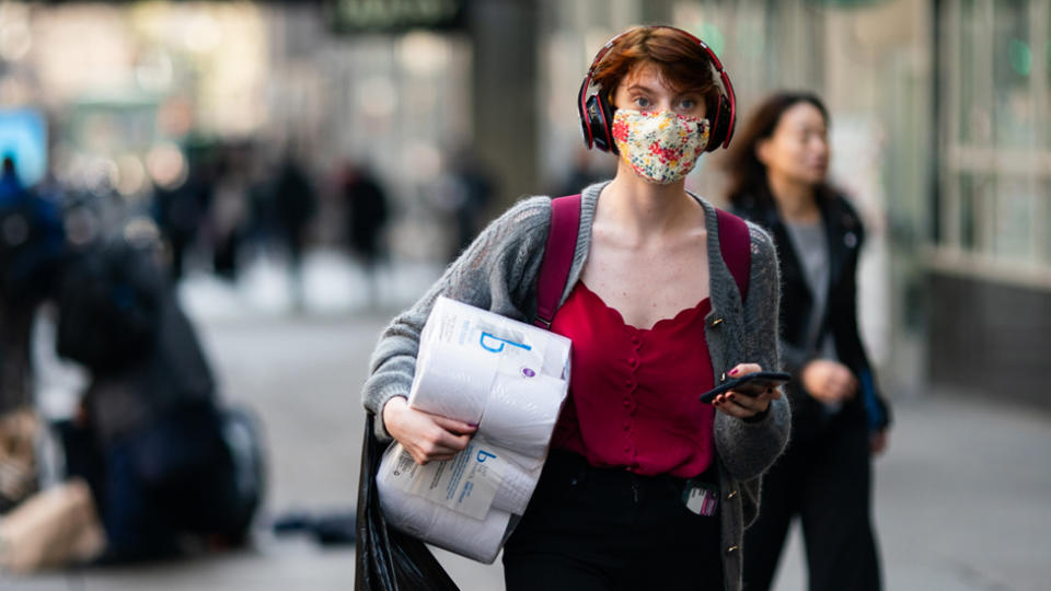 A woman wearing a mask carrying toilet paper during the coronavirus pandemic.