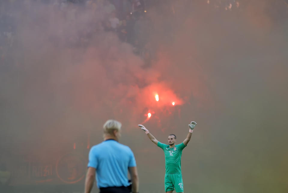 Serbia's goalkeeper Predrag Rajkovic gestures on the pitch as Romanian fans light flares during the UEFA Nations League soccer match between Romania and Serbia on the National Arena stadium in Bucharest, Romania, Sunday, Oct. 14, 2018. (AP Photo/Vadim Ghirda)