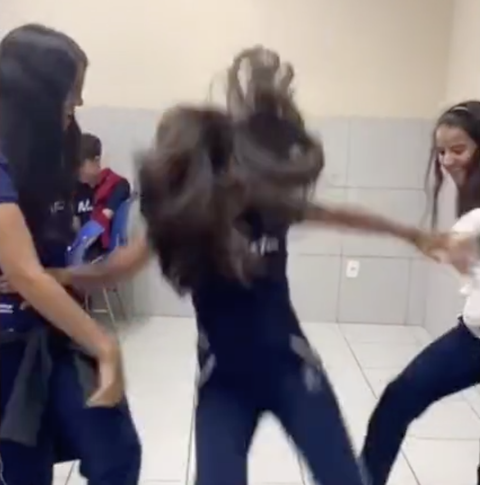 Two girls shown teaming up to kick the legs of another girl so she falls back onto the tiles. Source: TikTok via Facebook