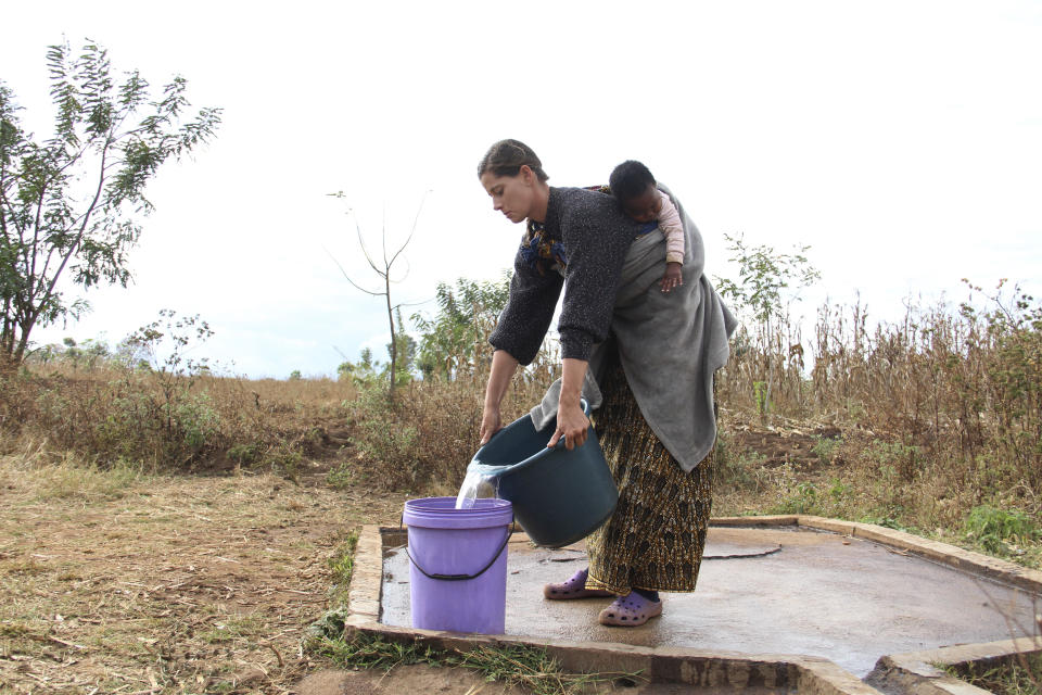 Cameron Beach, carries a child on her back as she collects water from a communal borehole in Dedza, near Lilongwe, Malawi, Friday, July 23, 2021. Beach, a former Peace Corps volunteer, is living in rural Malawi teaching English at a rural high school where she had been sent by the United States government 18-months before COVID-19 began sweeping the world. (AP Photo/Roy Nkosi)