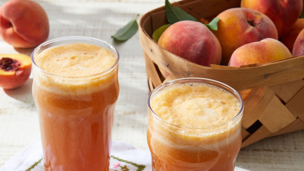 a couple of glasses with peach shandy in them next to a bowl of peaches