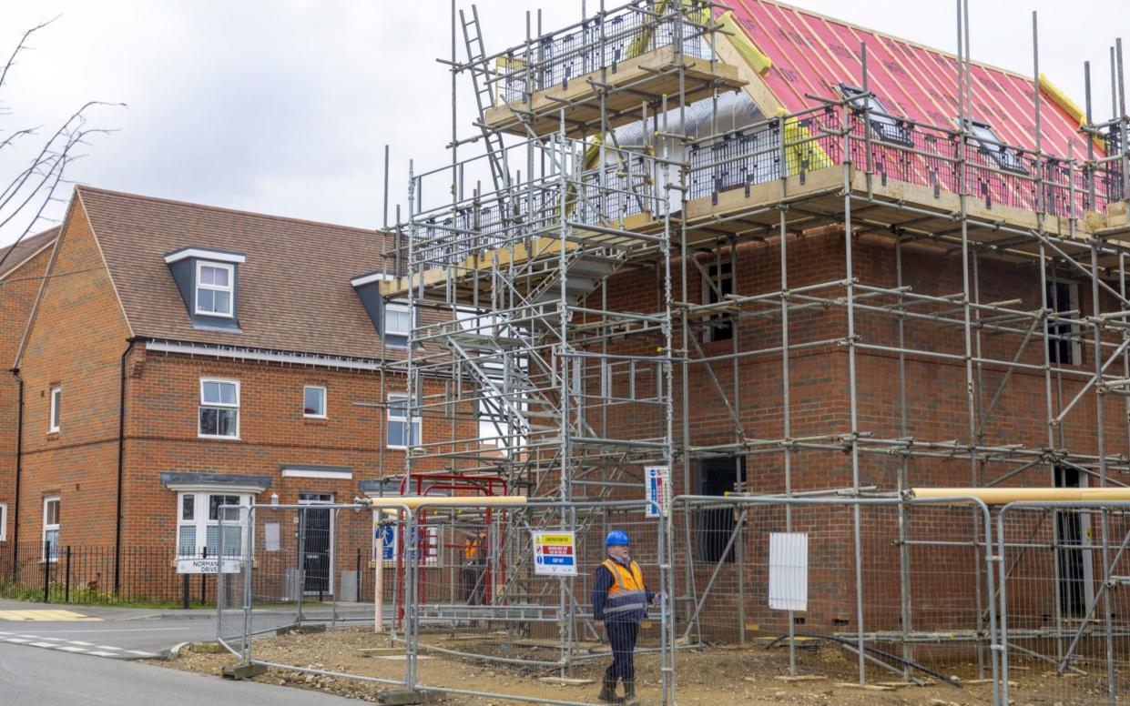 A builder passes through a residential property construction site in Surrey - Jason Alden/Bloomberg