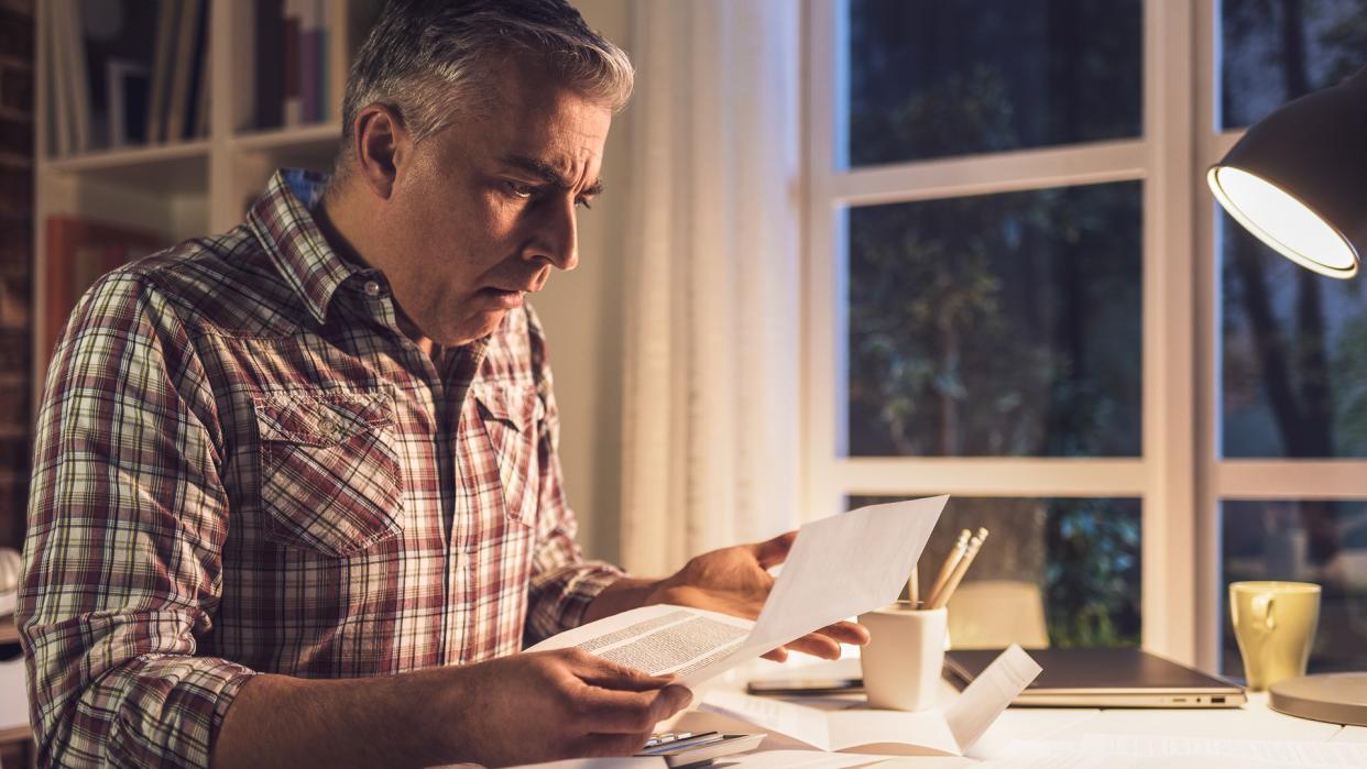 Shocked gasping man checking his domestic bills at home, he is holding an invoice and checking financial statements.