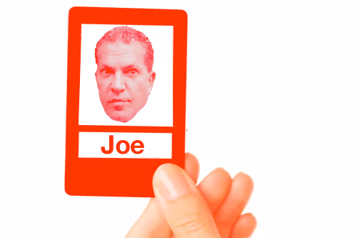 A hand holding a "Guess Who?" game card with Joe Tacopina's face on it.