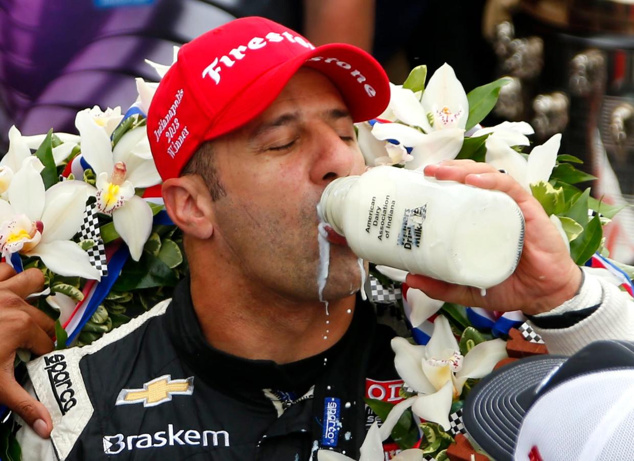 racecar driver wearing red firestone cap with wreath of flowers over shoulders chugs milk from a glass bottle