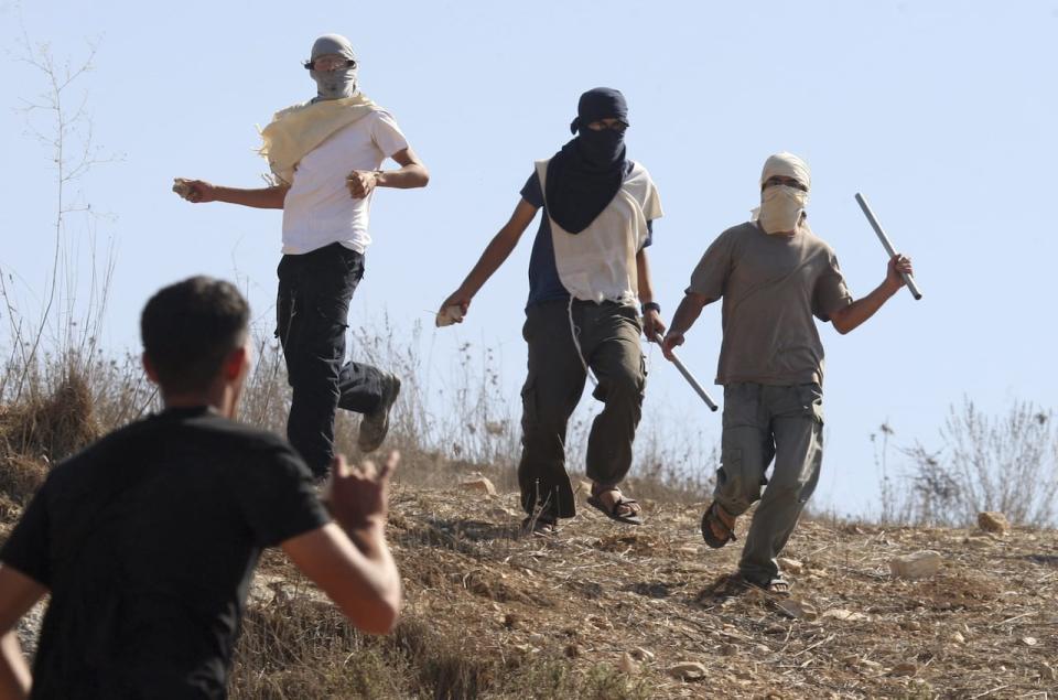 Masked Jewish settlers, top, clash with Palestinians in the West Bank village of Assira al-Kibliya on Sept. 20, 2011. On Thursday, Jan. 5, 2012, the Israeli military has banned 12 Jewish extremists from the West Bank for three to nine months because they are suspected in violence against Palestinians and Israeli soldiers.