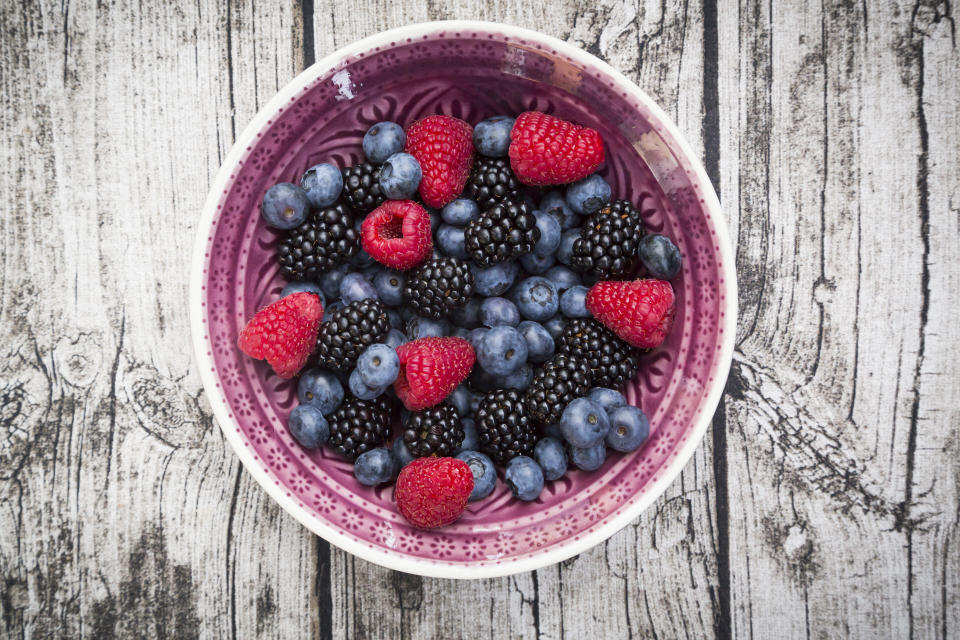 A bowl of fresh berries including raspberries, blackberries, and blueberries, placed on a rustic wooden surface