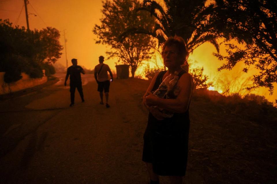 A local resident holds bottles of water next to a wildfire burning in the village of Latas, in southern Greece, on Saturday (Reuters)