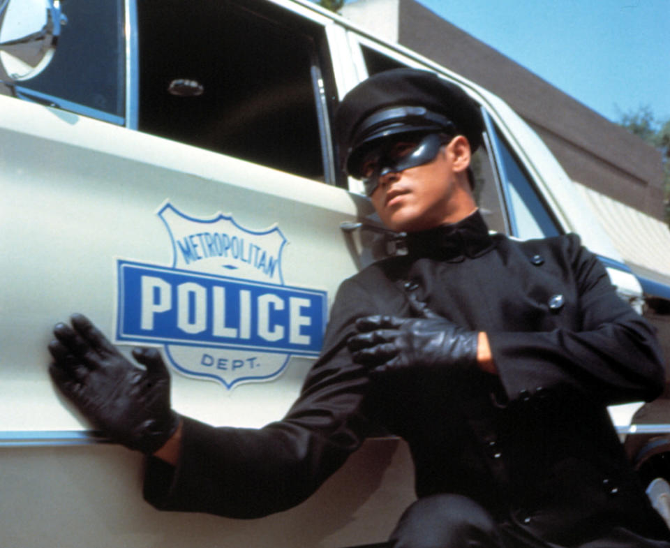 Bruce Lee as Kato in a fighting stance beside a police car