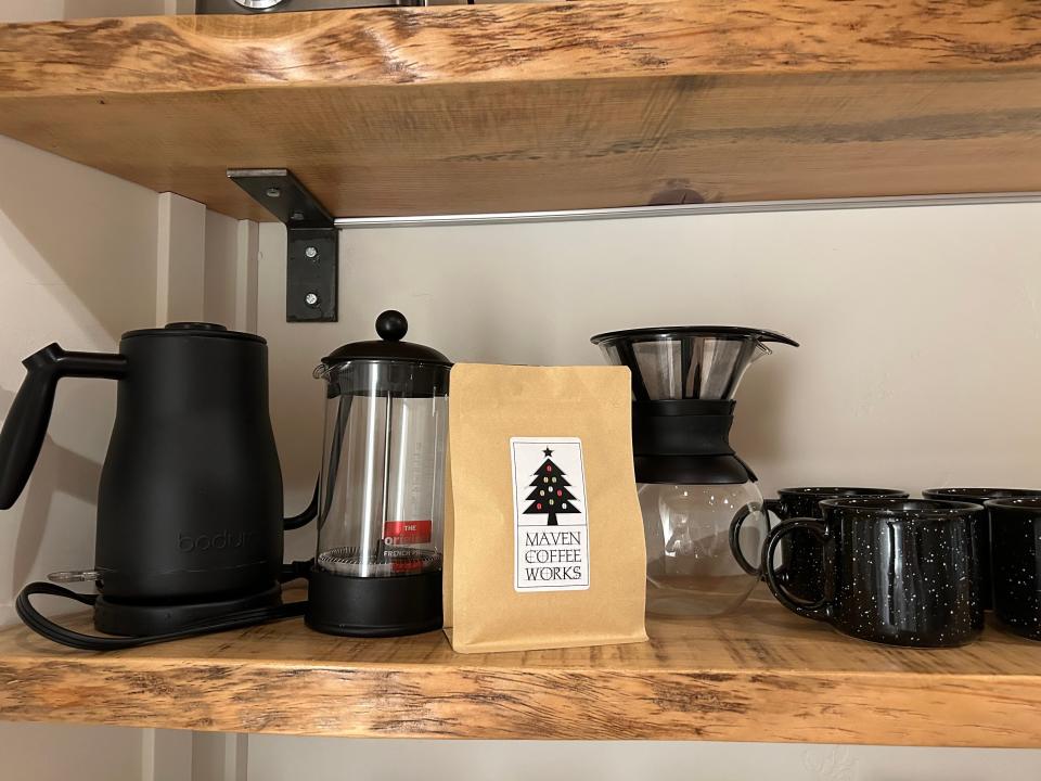 A bag of coffee beans in front of a pour-over coffee pot, a French press, and coffee mugs.