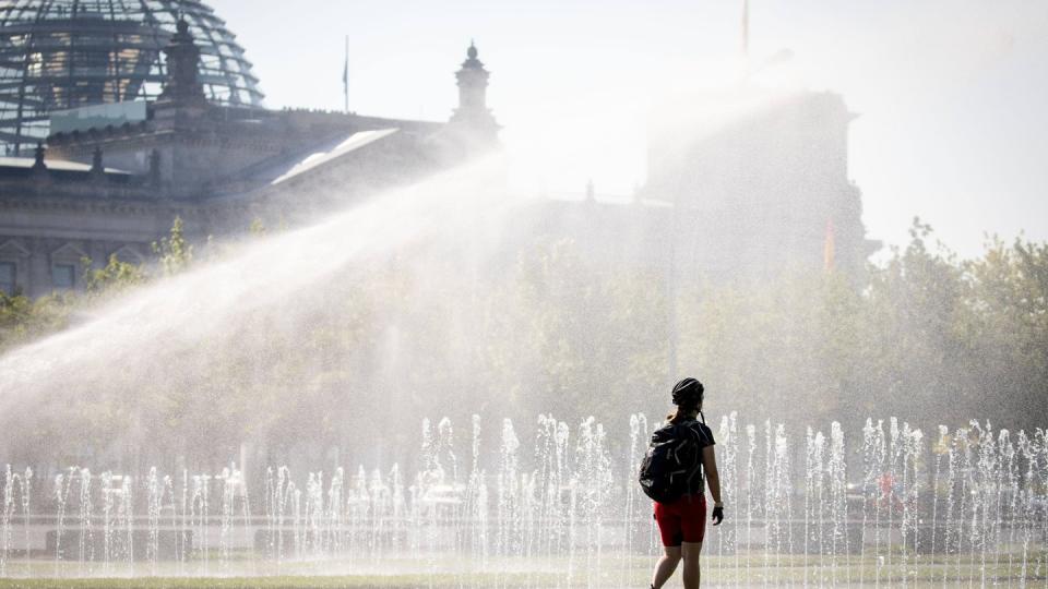 Eine Passantin erfrischt sich in einer Wasserfontäne vor dem Reichstag in Berlin. Nicht nur die Hauptstadt schwitzt. Foto: Kay Nietfeld