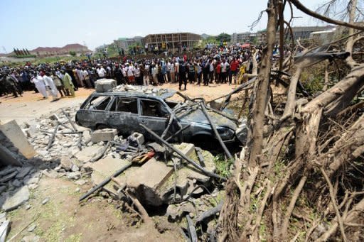 People gather around a vehicle destroyed in a suicide attack outside ThisDay Newspapers in Abuja. At least eight people were killed in the attack and in a car bombing at another of its offices