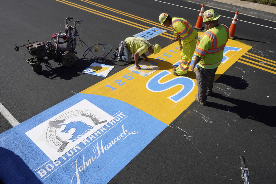 FILE - Painter Will Belezos, of Holbrook, Mass., left, uses a stencil, Wednesday, Oct 6, 2021, while working to complete the start line for the 125th edition of the Boston Marathon, in Hopkinton, Mass. Once a year for the last 100 years, Hopkinton becomes the center of the running world, thanks to a quirk of geography and history that made it the starting line for the world's oldest and most prestigious annual marathon. (AP Photo/Steven Senne, File)
