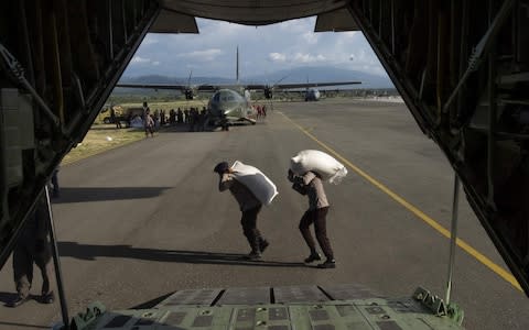 Indonesian policemen carry sacks of aid supplies  - Credit:  YUSUF WAHIL/ AFP