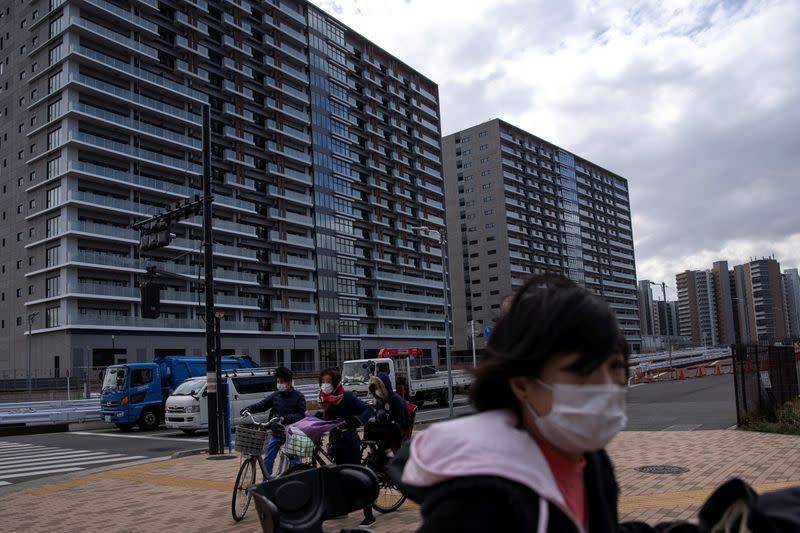 People wearing face masks, following an outbreak of the coronavirus, ride their bicycles past an under-construction site of the Tokyo 2020 Olympics villages in Tokyo