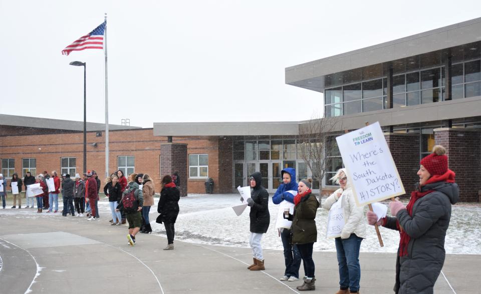 Teachers at North Middle School in Harrisburg stand in the cold as part of a "walk-in" to school to stand against the proposed social studies standards on Wednesday morning, Nov. 16, 2022. Nicole Ruud, right, holds a sign bearing the message "Where's the South Dakota history?"