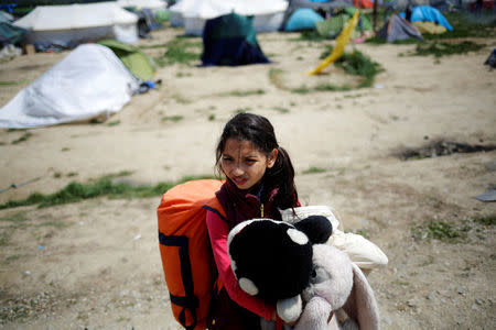 A girl holds a toy as she stands in front of tents at a makeshift camp for migrants and refugees at the Greek-Macedonian border near the village of Idomeni, Greece, April 22, 2016. REUTERS/Stoyan Nenov