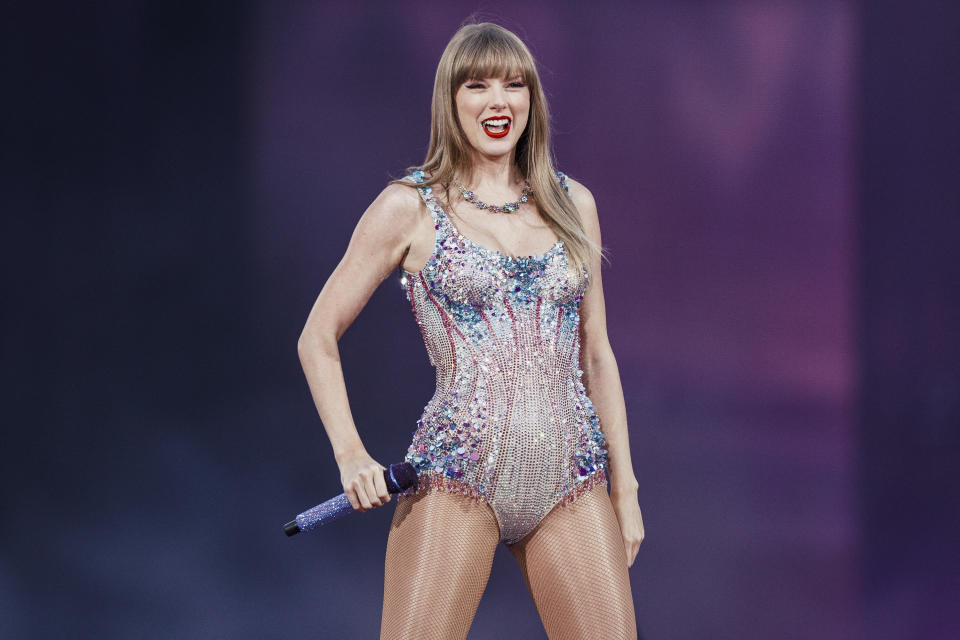 Taylor Swift performs on stage, wearing a sparkling, embellished bodysuit and holding a microphone