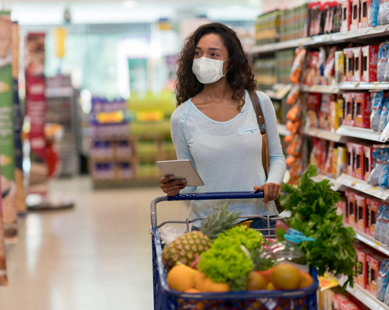 Woman shopping at the supermarket wearing a facemask to avoid the coronavirus while following a list on her tablet computer â COVID-19 lifestyle concepts  