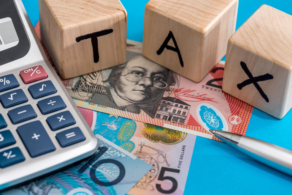 Wooden blocks spelling out tax with Australian bank notes, pen and calculator.