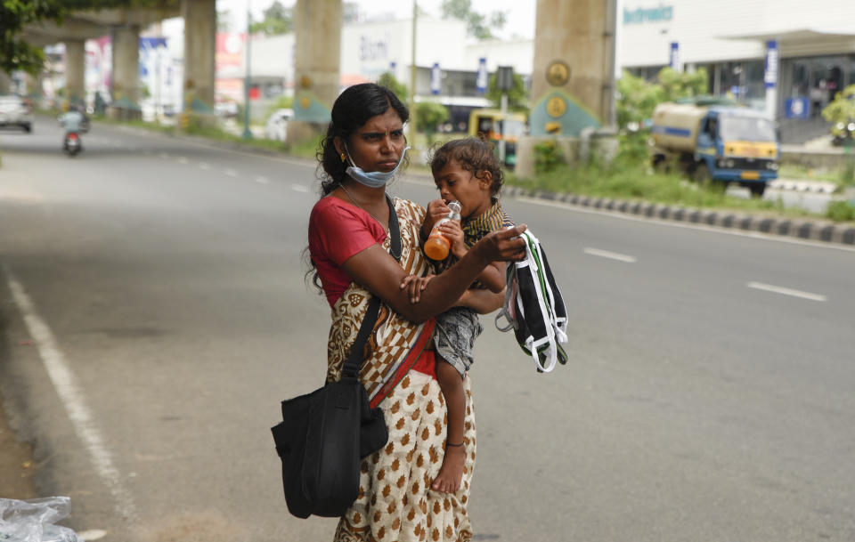 An Indian woman stands carrying her child by a roadside as she sells face masks during lockdown to curb the spread of coronavirus in Kochi, Kerala, India, Saturday, May 16, 2020. Over 90% of India's workforce is employed in the informal sector, without access to significant savings or social protection benefits such as paid sick leave or insurance. (AP Photo/R S Iyer)