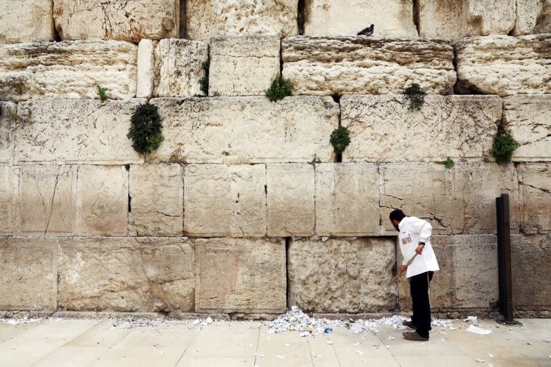 A man clears notes placed in the cracks of the Western Wall to create space for new notes ahead of the Jewish holiday of Passover, in Jerusalem's Old City