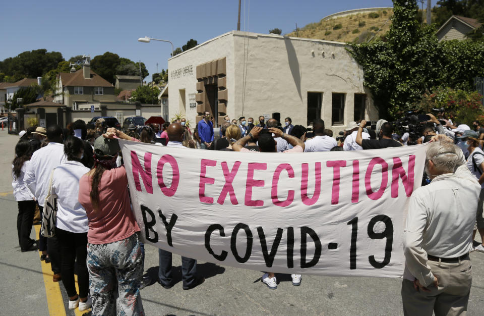 FILE - In this July 9, 2020, file photo, people hold up a banner while listening to a news conference outside San Quentin State Prison in San Quentin, Calif. The group of legislators, advocates, academics and public health officials gathered outside San Quentin State Prison to discuss a COVID-19 outbreak at the facility that has sickened more than 1,400 inmates with six deaths. A California appeals court has ordered state corrections officials to cut the population of one of the world's most famous prisons to less than half of its designed capacity, citing officials' "deliberate indifference" to the plight of inmates during the coronavirus pandemic. State prison officials said Wednesday, Oct. 21, 2020, that they are deciding whether to appeal the order, which otherwise will force them to parole or transfer about 1,100 inmates serving time in San Quentin State Prison north of San Francisco. (AP Photo/Eric Risberg, File)