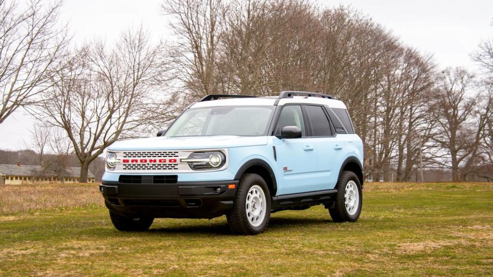 a blue four door suv with a white grille is parked on a field with some trees in the background