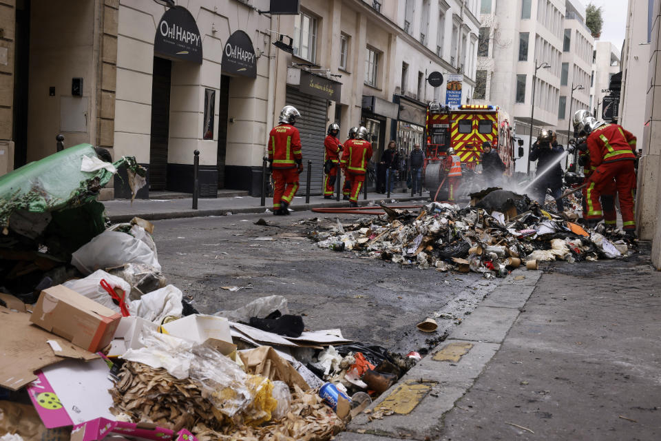 Firemen controlling the remains of a garbage fire from last night protests against the retirement bill in Paris, Friday, March 24, 2023. French President Macron's office says state visit by Britain's King Charles III is postponed amid mass strikes and protests. (AP Photo/Thomas Padilla)