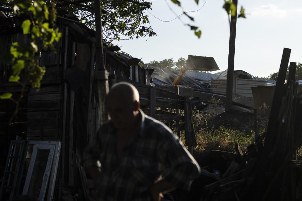 A resident, whose home is badly damaged in Russian missile attacks targeting a grain facility next to his home, pauses for a moment as a loader dumps salvageable grain into a transport truck at the facility in Pavlivka, Ukraine, Saturday, July 22, 2023. (AP Photo/Jae C. Hong)