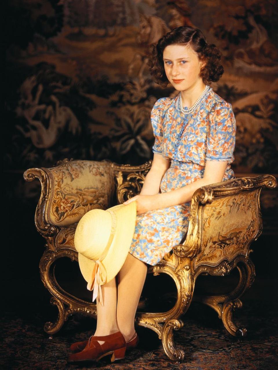 <p>Princess Margaret, seated and wearing a multi-colored dress and holding a straw hat.</p>