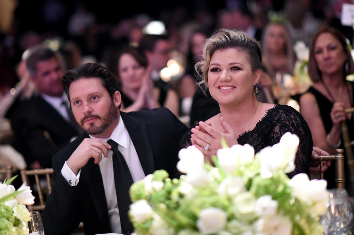 Kelly Clarkson and Brandon Blackstock in formal attire sit at a table. White flowers can be seen in the foreground. (Michael Buckner / Getty Images for Celebrity Fight Night)