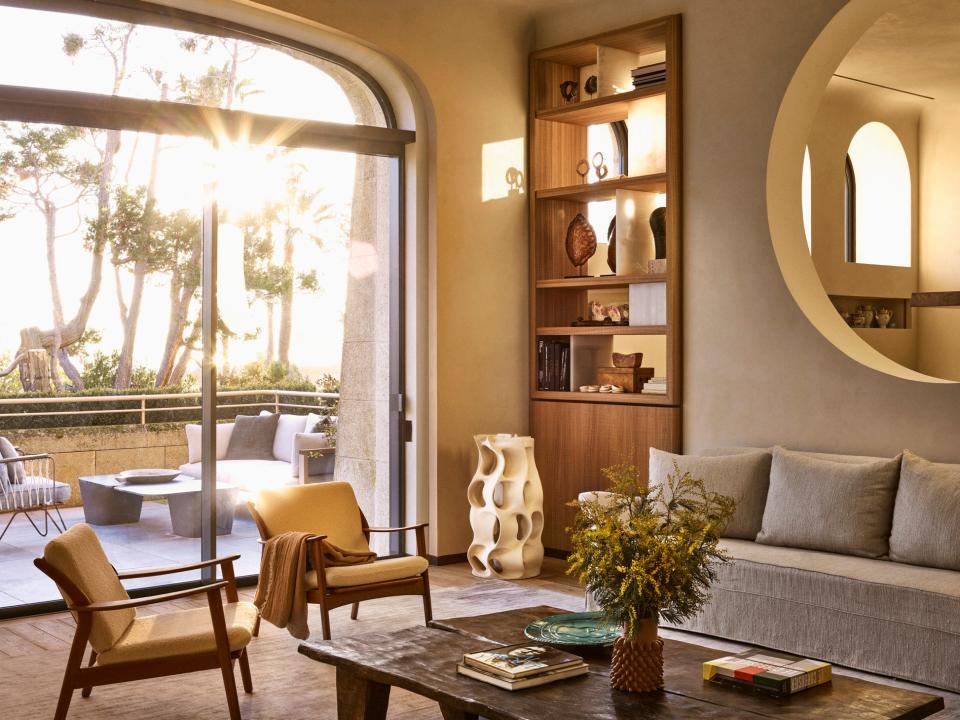 The lounge is furnished with two coffee tables. The blue ceramic plate is from Galerie Agnes Sandhal, while the ceramic pine vase is by Studio Floris Wubben. Guy Bareff designed the white ceramic floor lamp. The custom beige sofas are by Caprini & Pellerin Architectes. In the nearby lounge terrace, armchairs by Honoré Deco and an outdoor coffee table beckon.