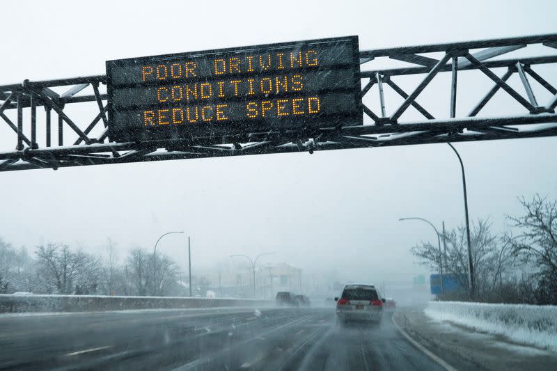 Cars drive under the snow while weather information is seen on a screen along the Jericho Turnpike in Mineola, New York