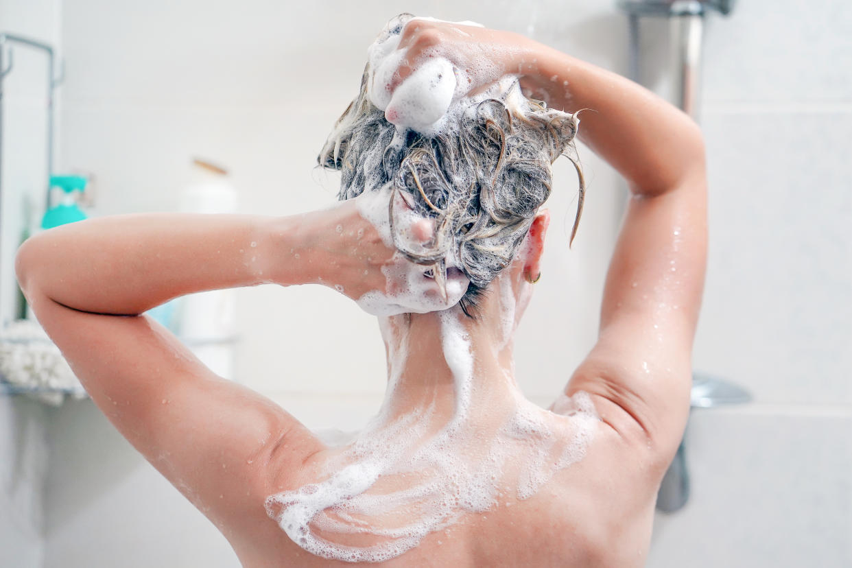 Woman washes her hair with shampoo in bathroom. Woman washing her hair with a lot of foam inside a shower. Back view of young woman washing her hair.