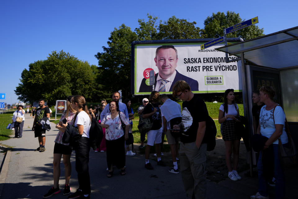 People wait for a bus by an election billboard for "SaS" (Freedom and Solidarity) party in Michalovce, Slovakia, Wednesday, Sept. 6, 2023. The billboard reads: 'SaS economic growth for the east'. Slovakia holds early parliamentary elections on Saturday Oct. 30, 2023, with a populist former prime minister Robert Fico and his scandal-tainted party "SMER" (Direction) favored to win after campaigning on a clear pro-Russian and anti-American message. (AP Photo/Petr David Josek)