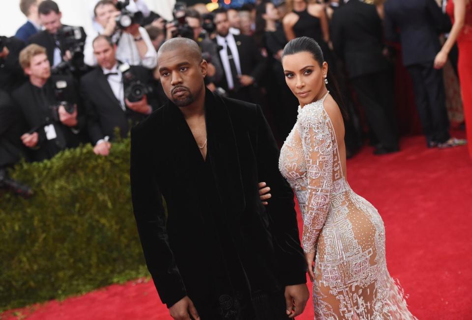 A man and a woman in formal attire walk on a red carpet surrounded by onlookers